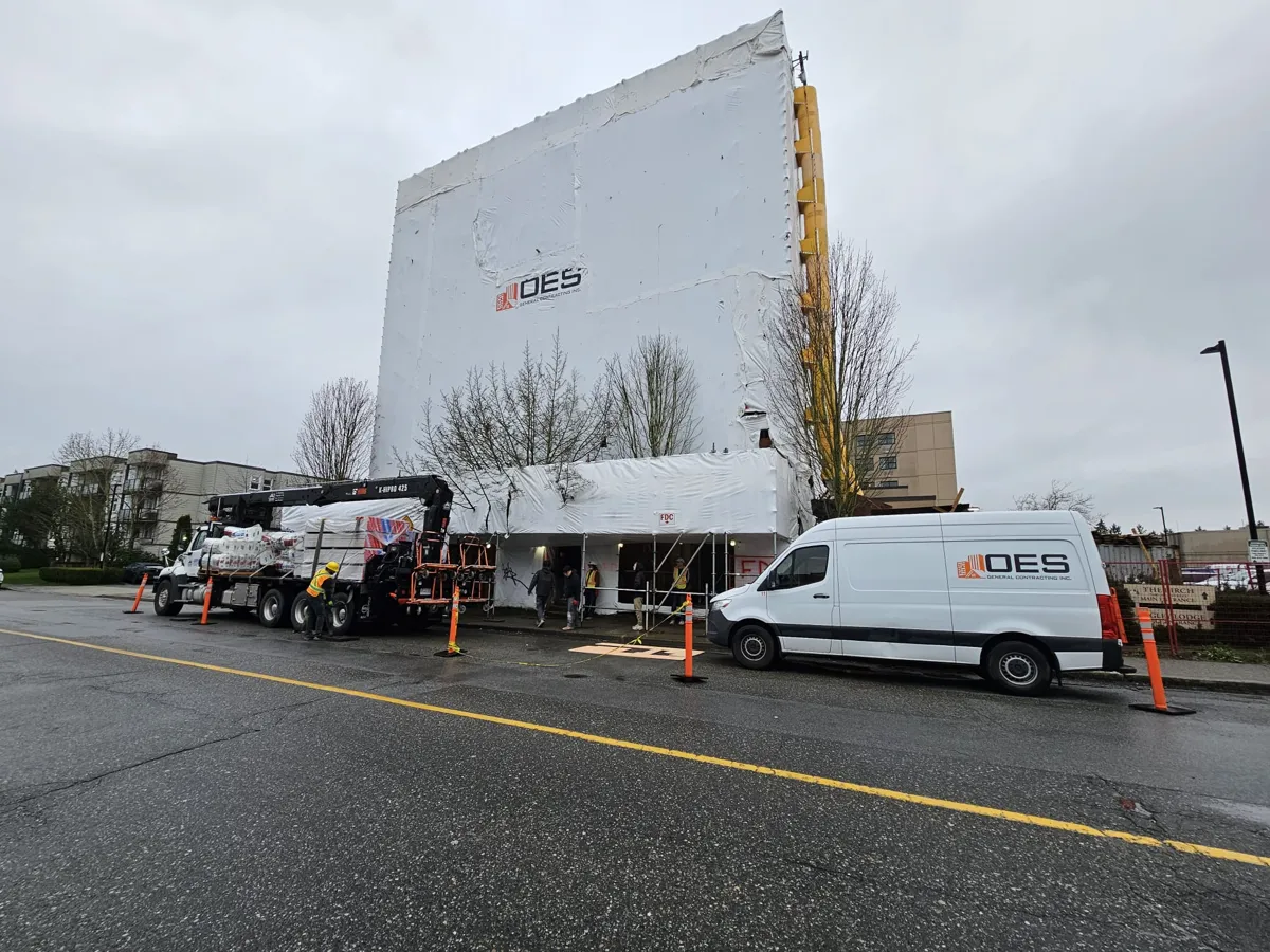 Six-storey building wrapped in white sheeting with an OES van and a delivery truck at the curb