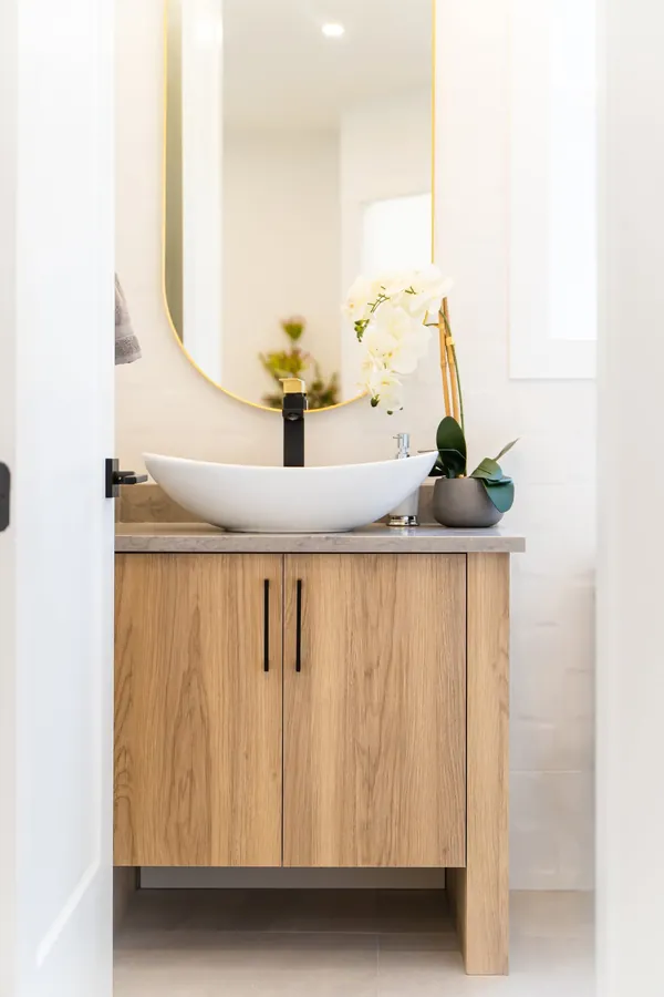 Powder room with a wood vanity, vessel sink and oval mirror