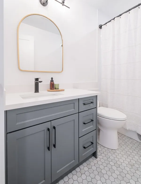 Bathroom with a blue vanity, arched mirror and hex tile floor