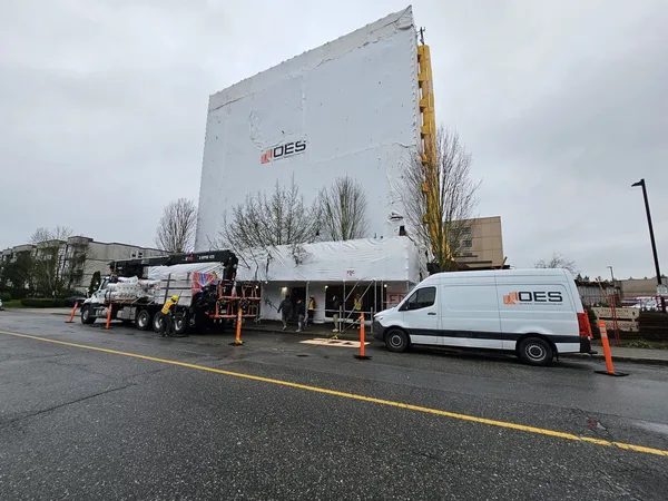 Six-storey building wrapped in white sheeting with an OES van and a delivery truck at the curb