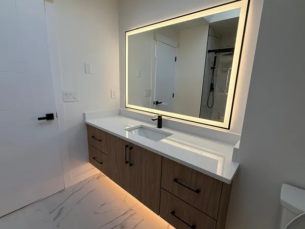 Bathroom with a wood floating vanity, quartz top and a large backlit mirror