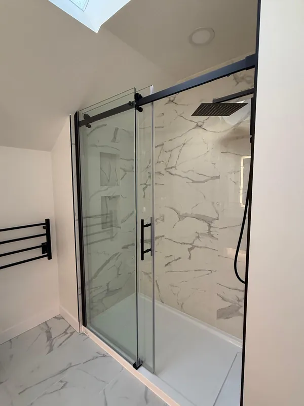 Shower with a sliding glass door, marble-look tile and a black rain shower head