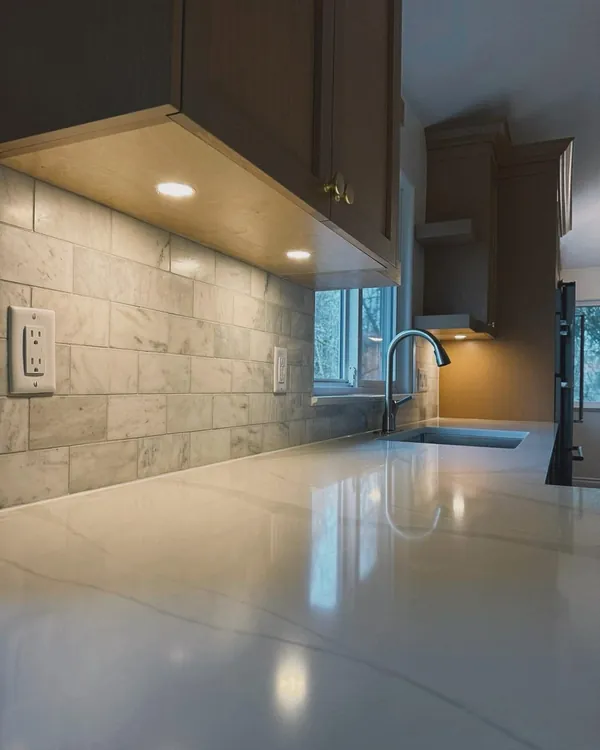 Under-cabinet lighting over a quartz counter and tile